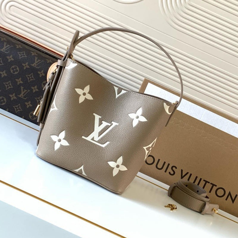 A Louis Vuitton taupe pebbled leather bucket bag with white monogram prints, displayed next to its brown monogram canvas pouch and a Louis Vuitton box on a white surface.