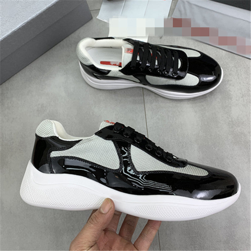 Black and white sneakers held by a hand on a gray floor.