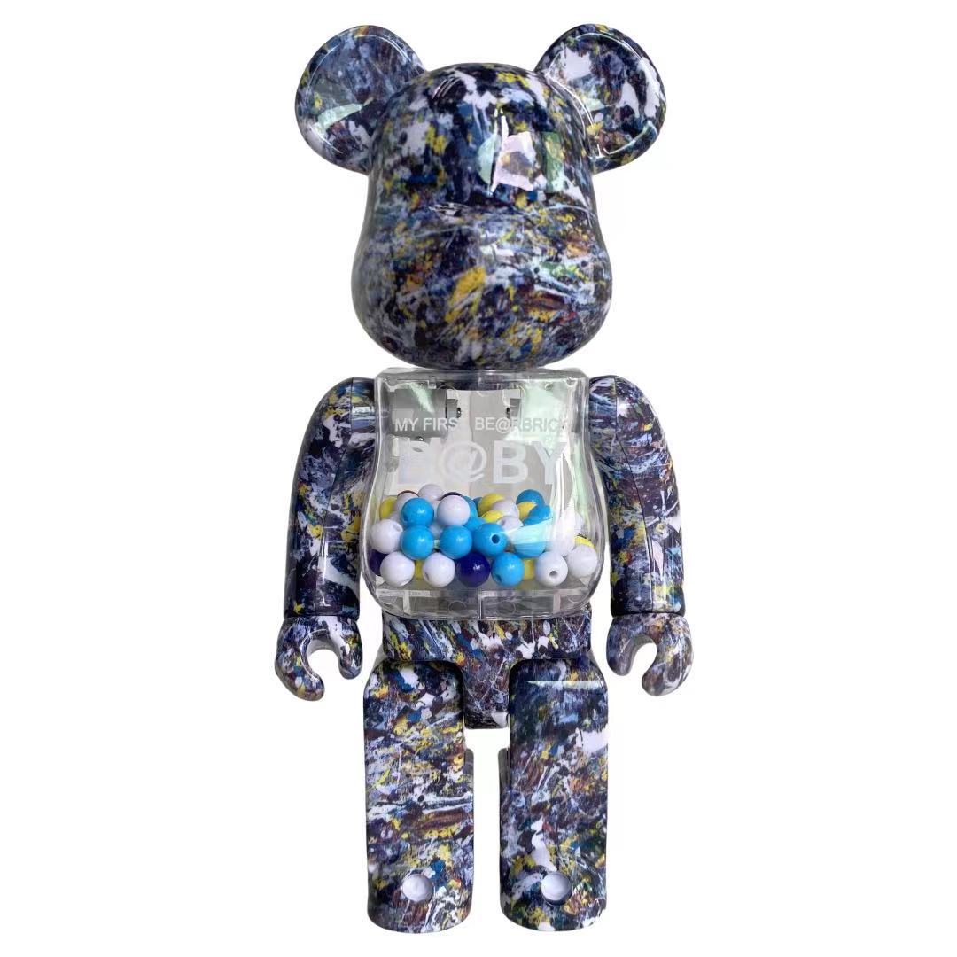 A Bearbrick-style collectible figure with a marbled blue, black, white, and yellow patterned body, featuring a transparent chest compartment filled with blue, white, and yellow beads. The figure is centered on a plain white background.