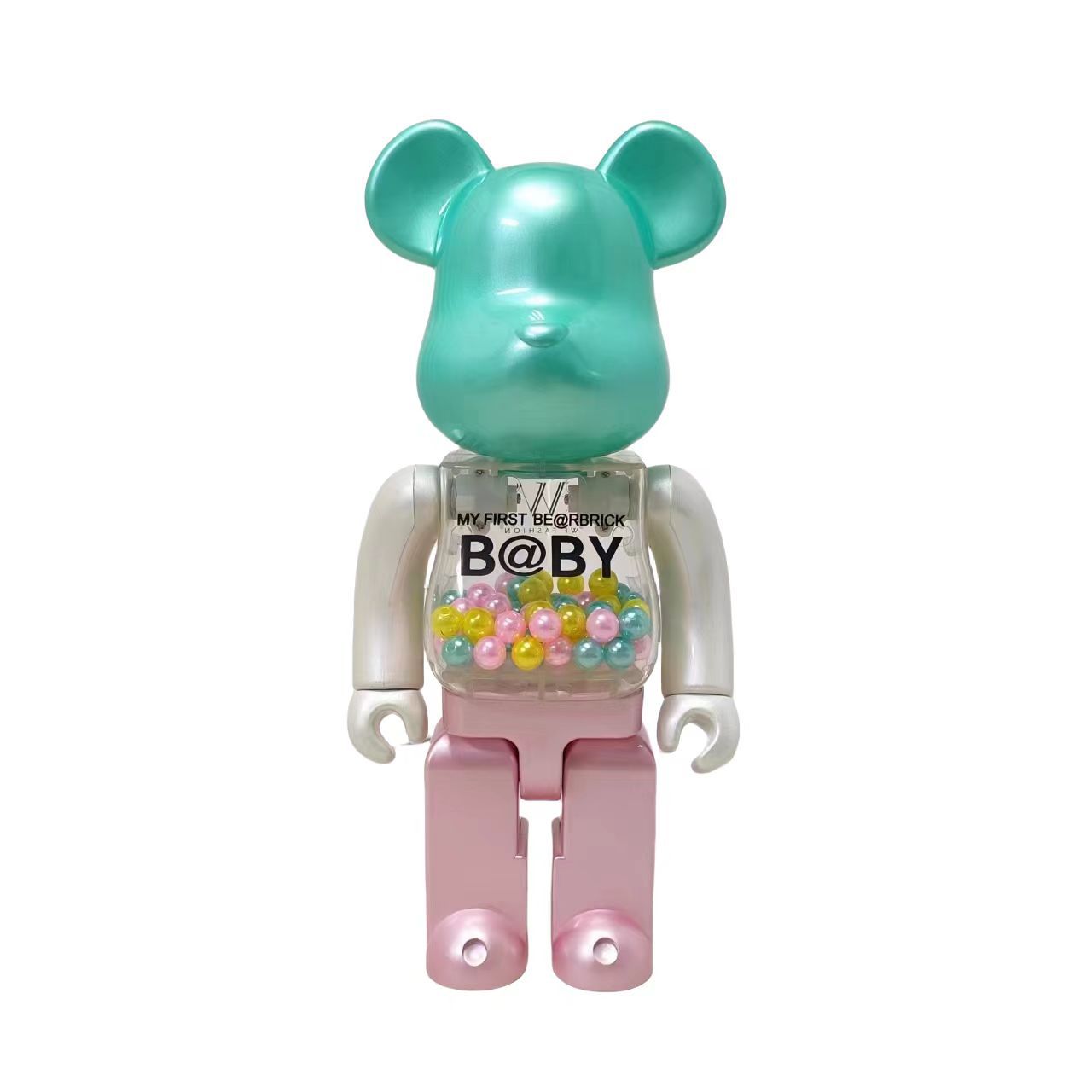 A Bearbrick collectible figure with a metallic teal head, white arms and hands, and pink legs. Its chest is a clear plastic container filled with small multicolored beads, with 'MY FIRST BEARBRICK B@BY' printed on the front.