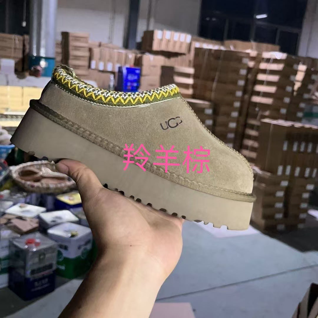 A beige suede slip-on platform shoe held in a hand, with a yellow and white chevron trim along the collar. The shoe features a chunky sole and a visible UGG logo on the side.