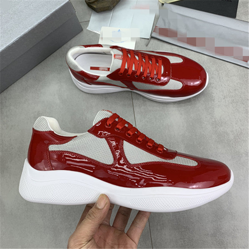 Red and white sneakers with a glossy finish, held by a hand on a gray floor.