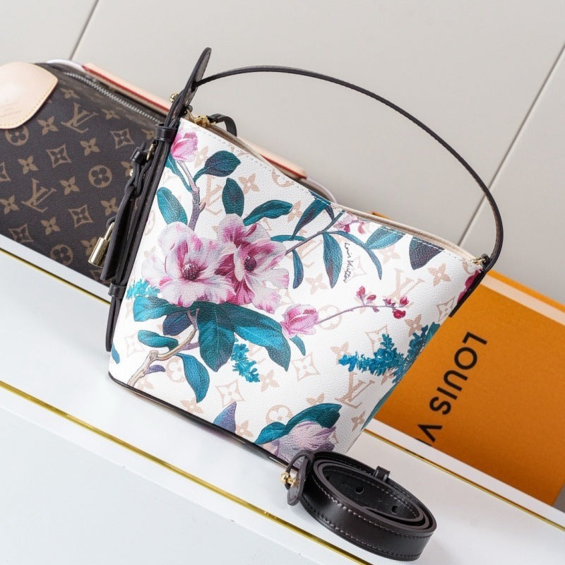 Louis Vuitton floral handbag with a white base, pink and purple flowers, and teal leaves, shown with a detached black strap on a white surface next to an orange Louis Vuitton box.