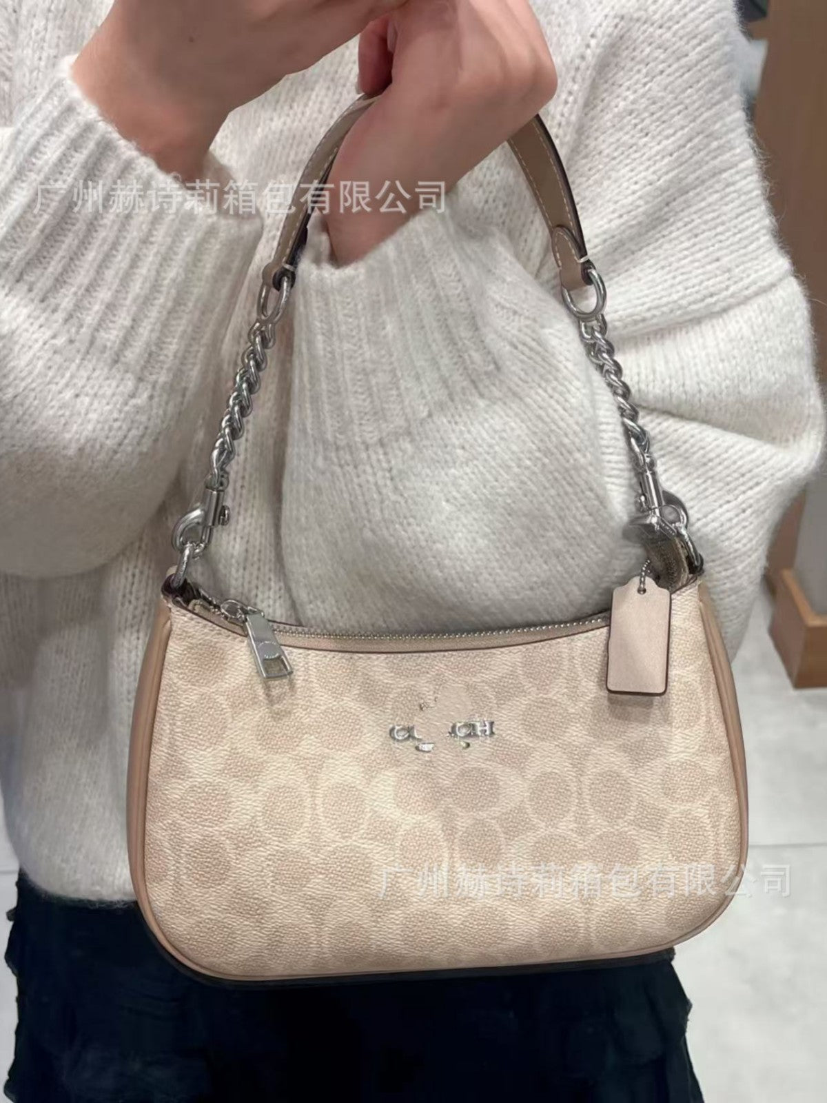 Beige handbag with chain strap held by a person wearing a white sweater.