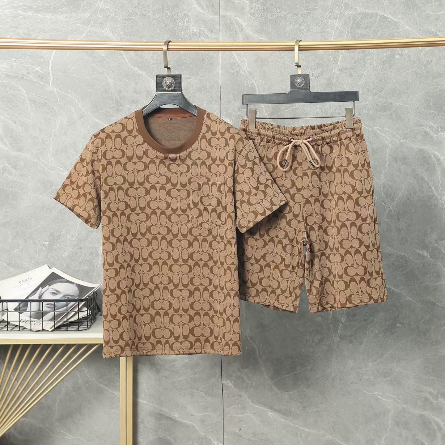 Brown patterned shirt and shorts set hanging on a rack against a gray wall.
