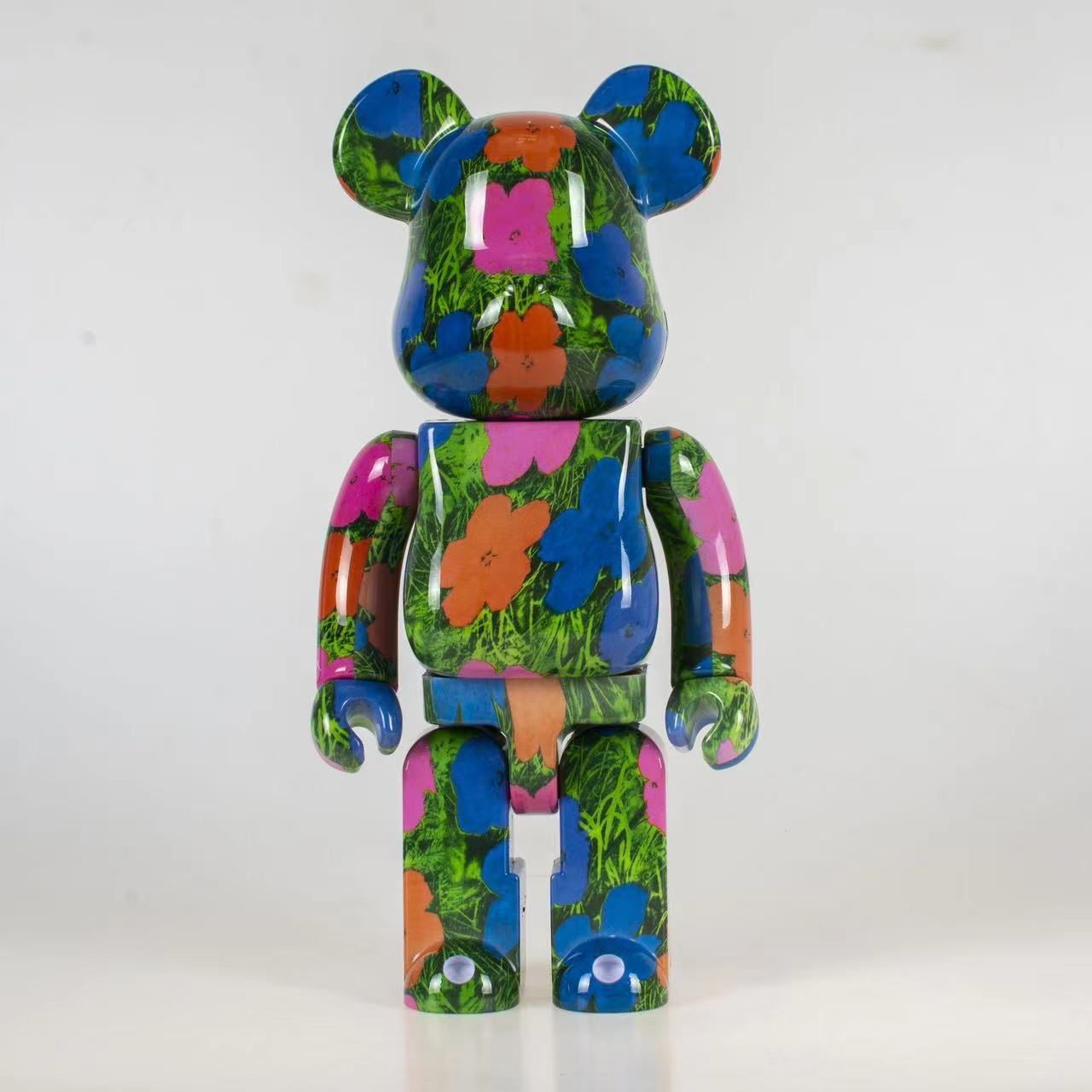 A bear-shaped collectible figure with a glossy multicolor floral pattern featuring blue, green, pink, orange, and purple on a white background.