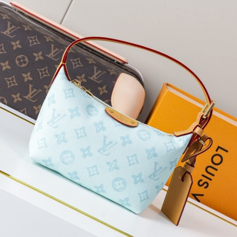 A light blue Louis Vuitton shoulder bag with the brand's monogram pattern, displayed next to a brown monogram pouch, an orange Louis Vuitton box, and a leather tag on a white surface.