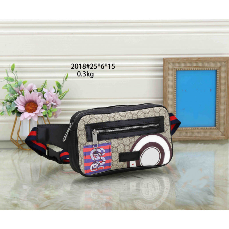 A beige and black patterned crossbody bag with red and black striped accents, displayed on a reflective surface with a floral vase and picture frame in the background. Text overlay reads '2018#25*6*15 0.