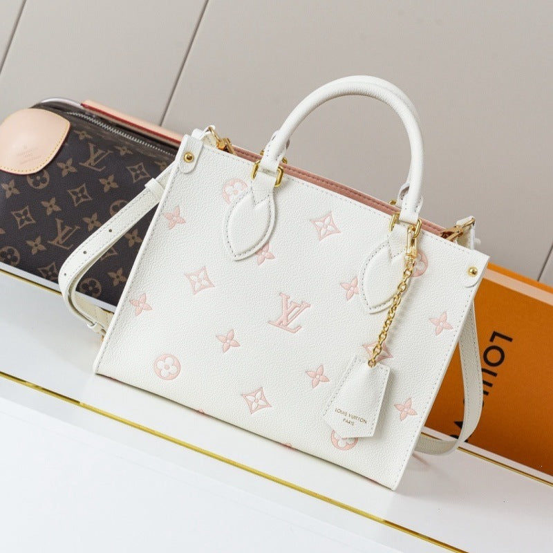 A white Louis Vuitton handbag with a light pink monogram pattern, gold-tone hardware, and a white leather top handle, displayed on a white surface next to a Louis Vuitton box and a brown monogram pouch.