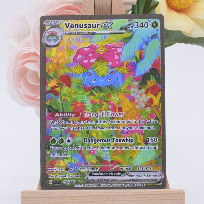 A holographic Venus ex Pokémon trading card displayed on a wooden stand, with soft pink and yellow flowers blurred in the background.