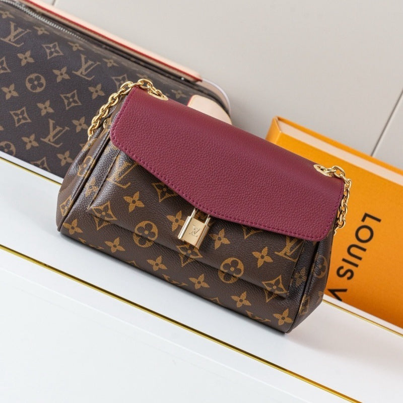 Louis Vuitton monogram shoulder bag with a burgundy leather flap and gold chain strap, displayed on a white surface next to an orange Louis Vuitton box.