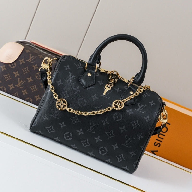 A Louis Vuitton black monogram handbag with gold-tone chain strap and top handles, displayed on a white surface with a Louis Vuitton box in the background.