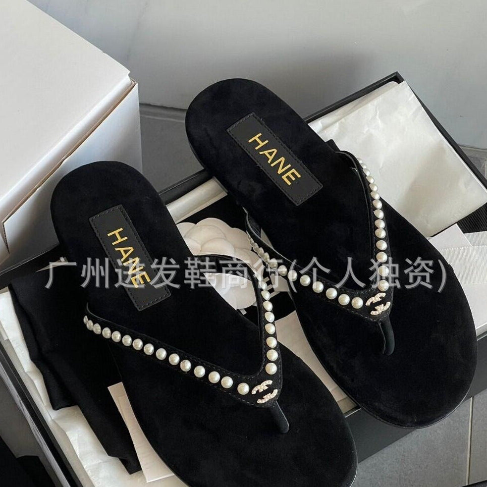 Black slippers with pearl embellishments on a white surface