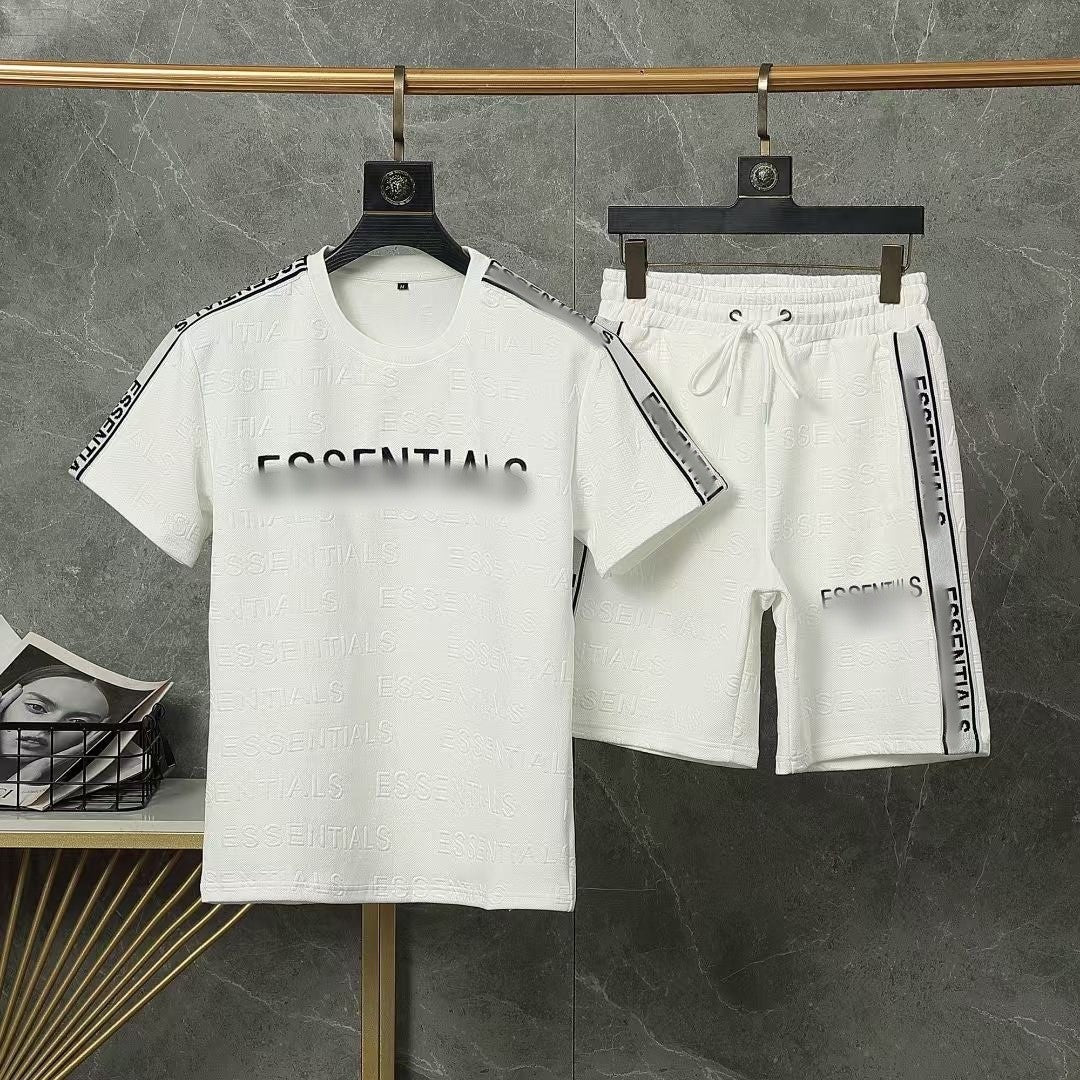 White t-shirt and shorts set with 'ESSENTIALS' text on hangers against a gray marble background.