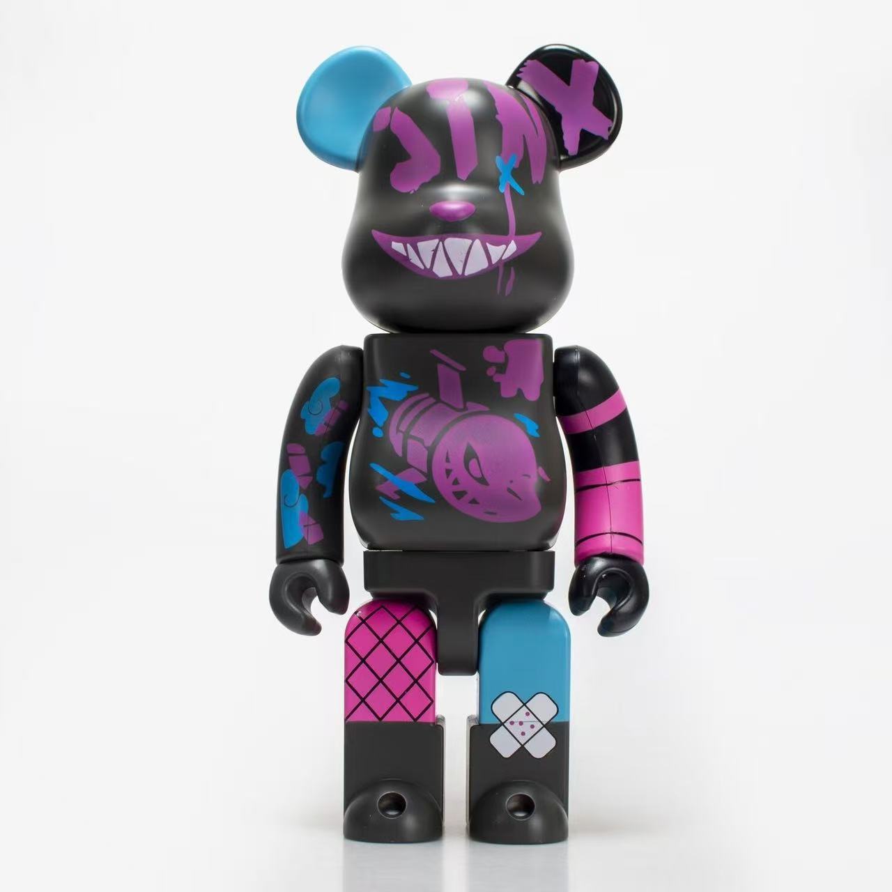 A collectible bear-shaped toy figure with a black body, purple graffiti-style face paint, blue and pink limbs, and a skull graphic on the chest, photographed against a clean white background.