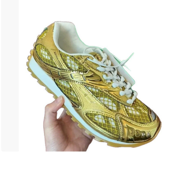 Gold sneaker with white laces held by a hand on a white background