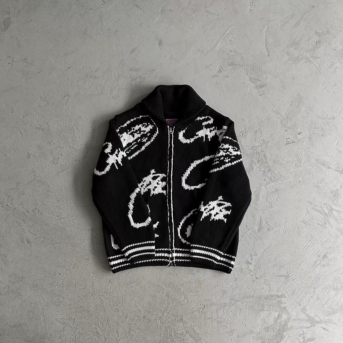 Black zip-up hoodie with white patterns on a gray surface