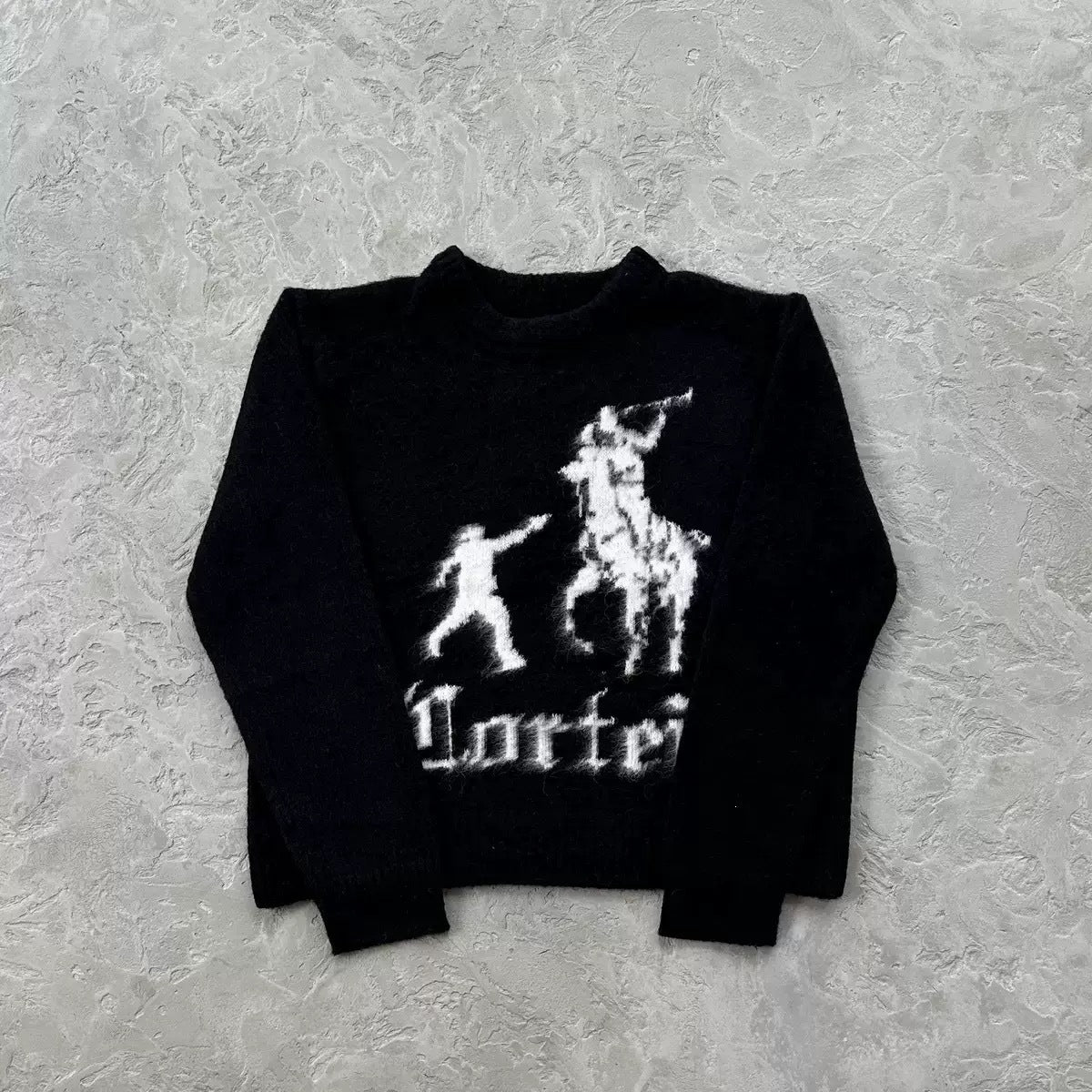 A black long-sleeve knit sweater with a white knitted graphic of a polo player and rider, and the word 'Lottei' in gothic font, laid flat on a textured gray background.