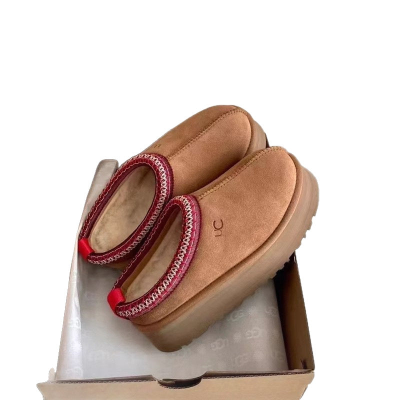 A pair of tan suede UGG platform slippers with red braided trim, resting inside their original cardboard shoebox on white tissue paper.