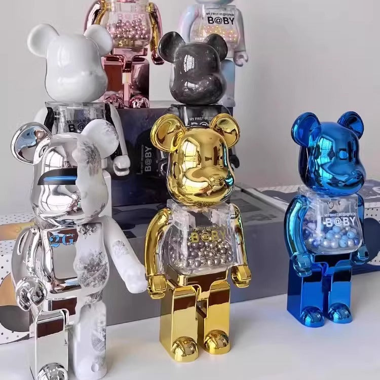 Four bear-shaped collectible figures with glossy metallic finishes in white, silver, gold, and blue, arranged together on a tabletop with their boxes in the background.
