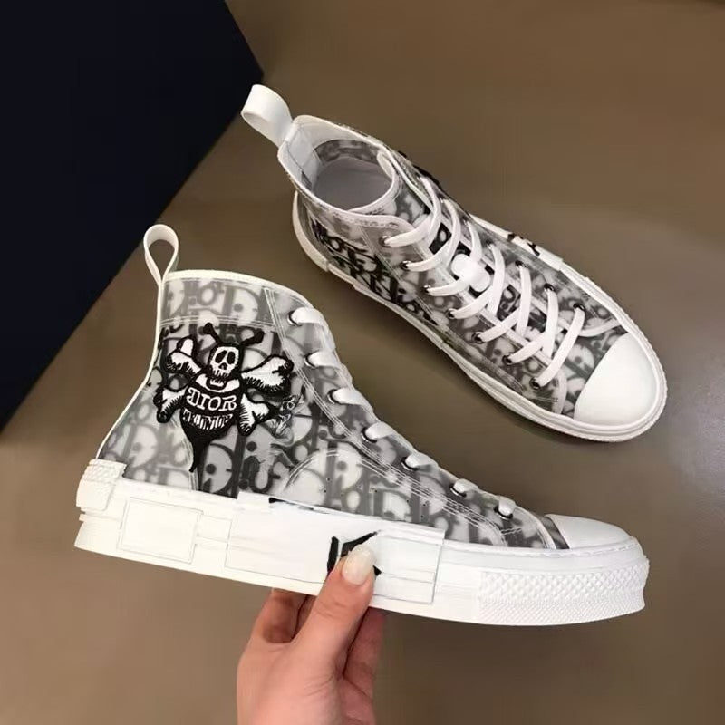High-top sneakers with skull design held by a hand on a neutral background