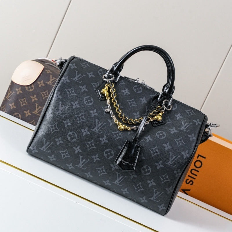 A Louis Vuitton monogram black leather handbag with gold chain accents and a black leather handle, displayed on a white surface next to an orange Louis Vuitton box.