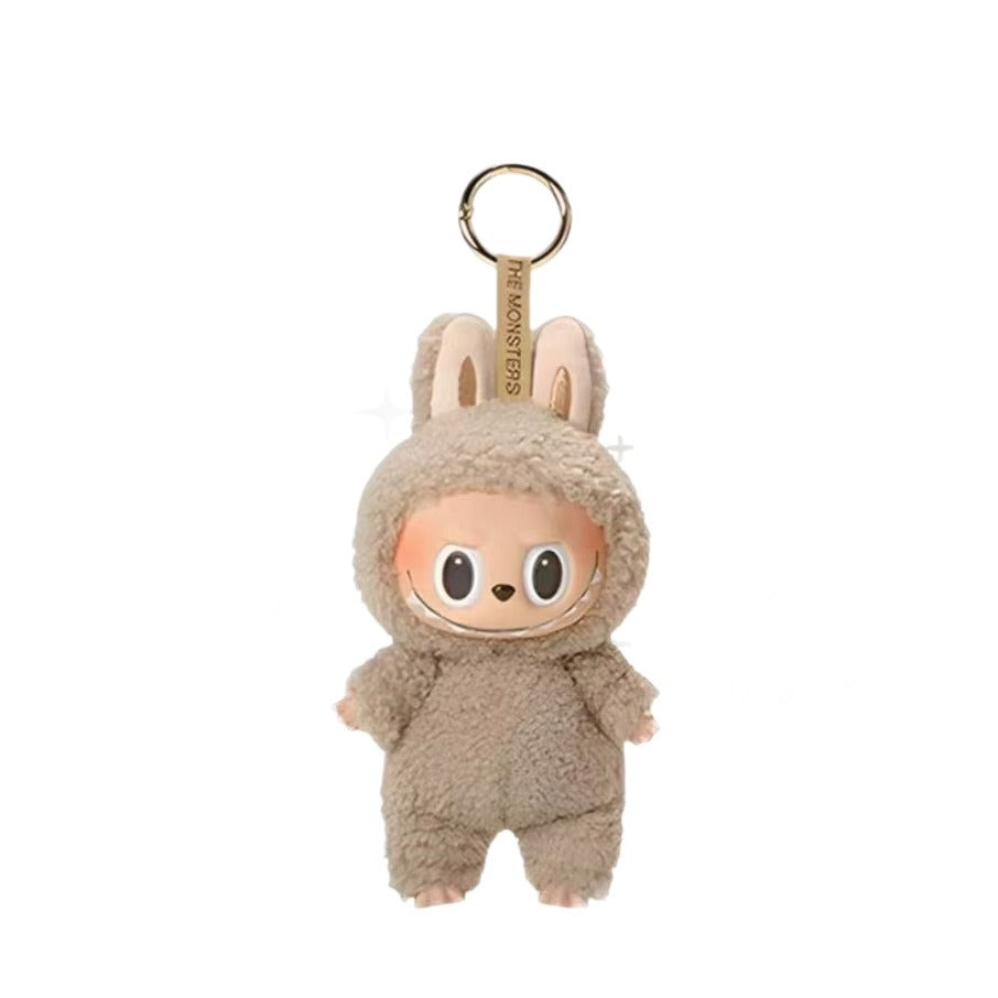 A plush character keychain in a fuzzy beige bunny suit with a gold-tone key ring and a hanging tag that reads 'THE MONSTERS'.
