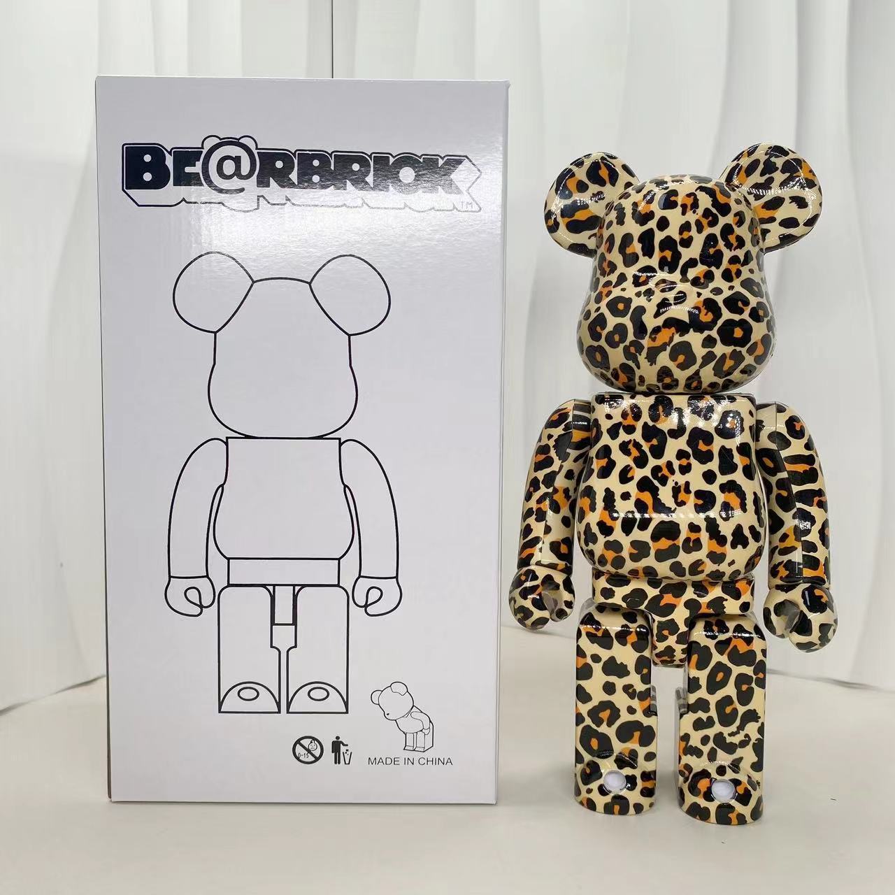A Bearbrick collectible figure with a beige, brown, and black leopard print stands next to its white product box, which features the BE@RBRICK logo.
