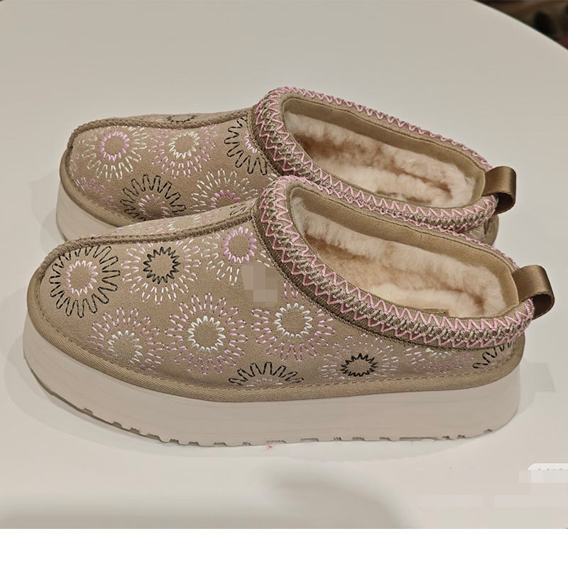 A pair of slip-on clogs with beige fabric uppers featuring embroidered circular floral patterns in pink, white, and black. The shoes have a soft, cream-colored fleece lining and thick white platform soles, shown on a plain white surface.