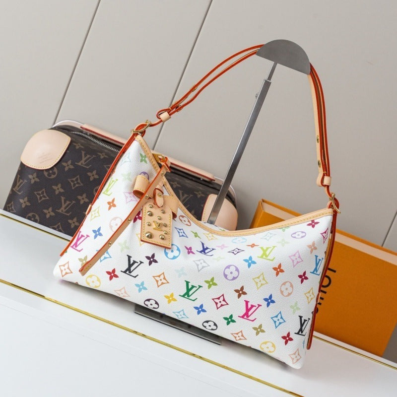 A Louis Vuitton shoulder bag in white canvas with a colorful monogram pattern, displayed on a stand next to a brown monogram handbag and an orange Louis Vuitton box.