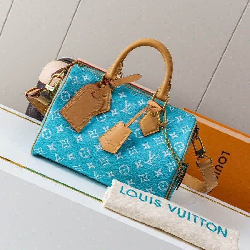 A Louis Vuitton monogram Speedy handbag in bright turquoise blue with tan leather handles and tags, displayed on a white shelf with a Louis Vuitton dust bag and orange box in the background.