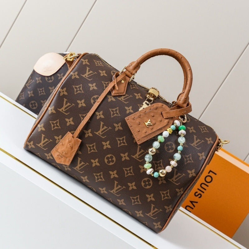 Louis Vuitton monogram canvas handbag with brown leather handles and trim, gold-tone hardware, a detachable beaded wristlet charm, and an orange Louis Vuitton box partially visible behind it on a white surface.