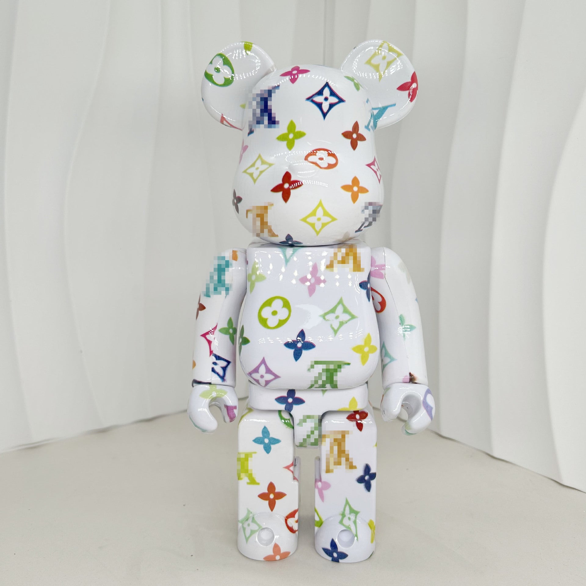 A white bear-shaped collectible figure covered in a colorful Louis Vuitton monogram pattern, photographed against a white draped studio backdrop.