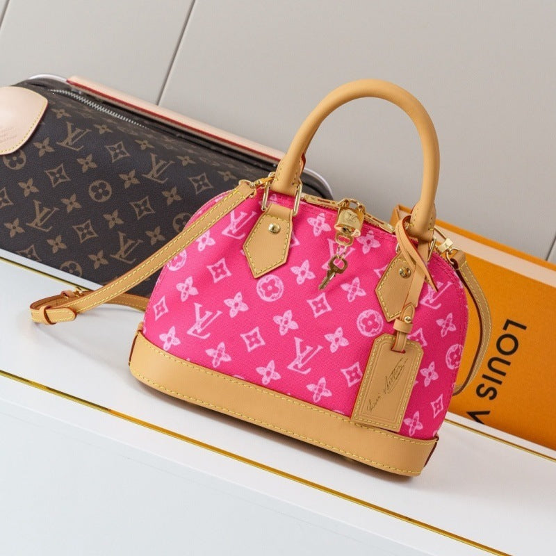 A Louis Vuitton Alma BB handbag in pink monogram canvas with tan leather trim and handles, displayed on a white surface next to a Louis Vuitton monogram pouch and an orange Louis Vuitton box.