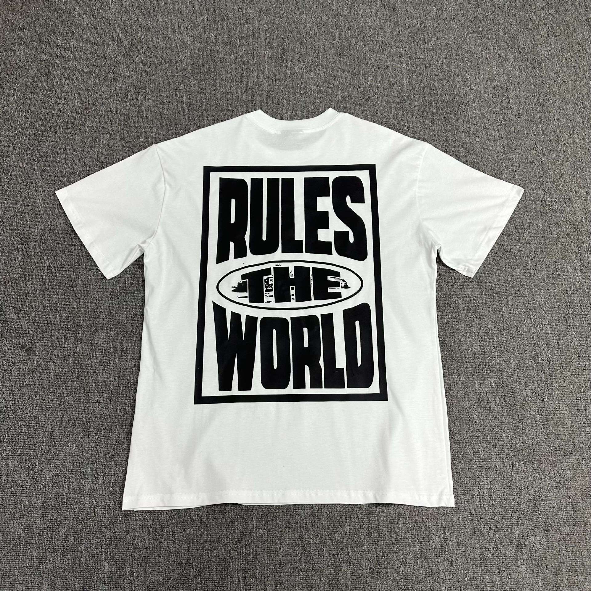 White t-shirt with 'RULES THE WORLD' text on a gray background