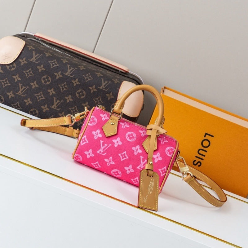 A pink Louis Vuitton monogram Speedy handbag with tan leather handles and strap, displayed next to a Louis Vuitton monogram pouch and an orange Louis Vuitton box on a white surface.