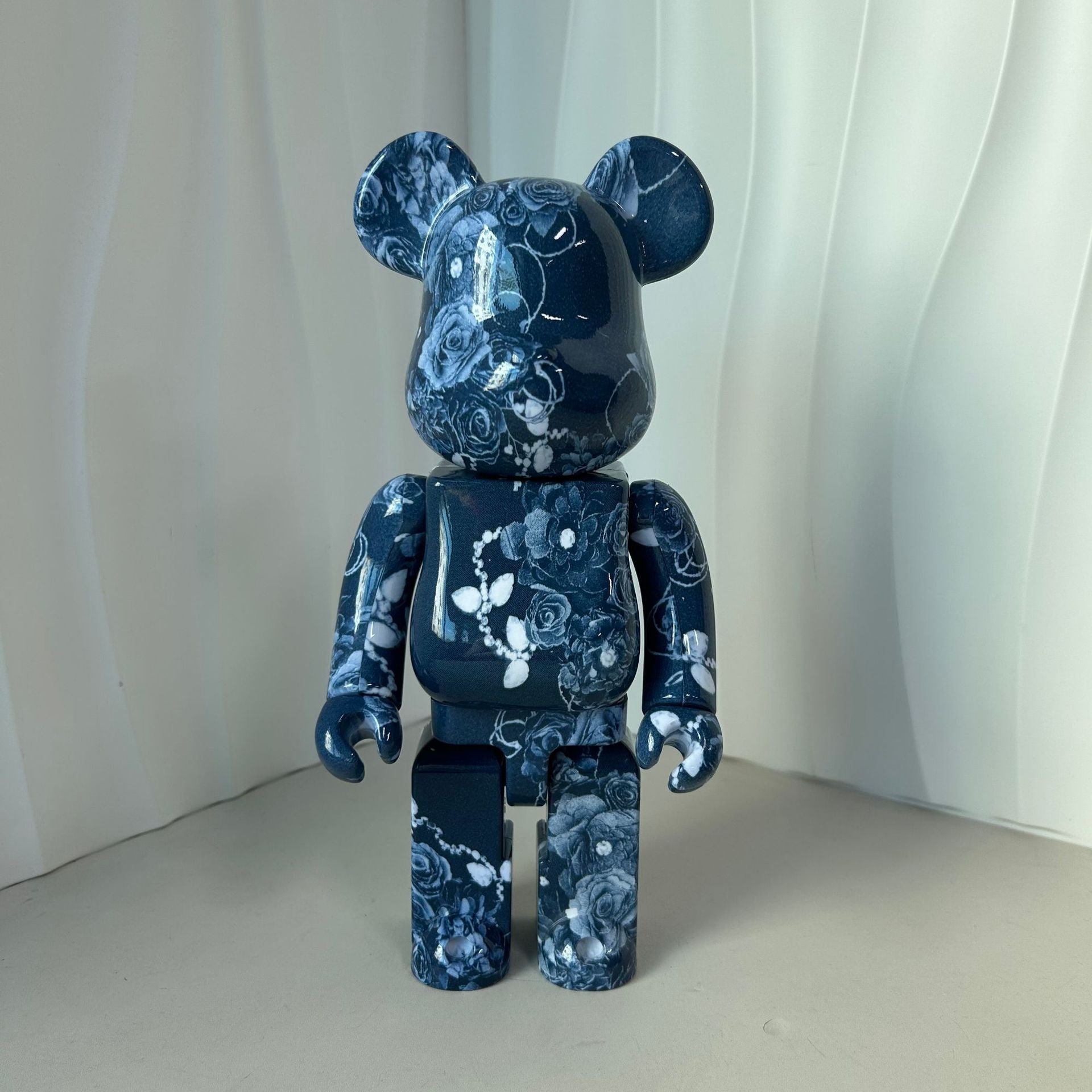 A collectible bear-shaped figure with a glossy dark blue and white floral pattern, standing against a white draped background.
