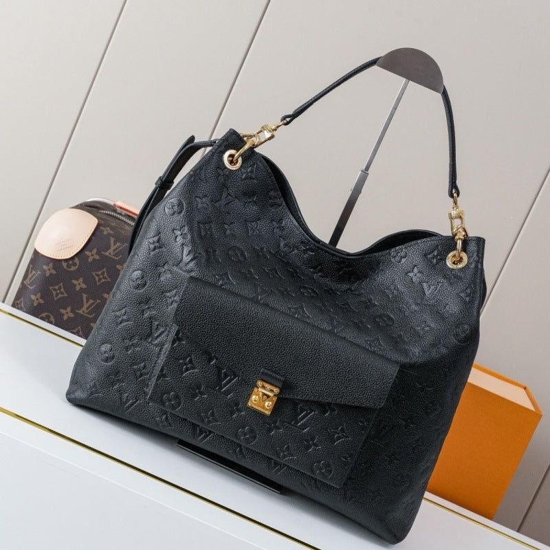 A black Louis Vuitton shoulder bag with embossed monogram pattern, gold-tone hardware, and a flap front, displayed on a white surface with a Louis Vuitton monogram pouch and orange box in the background.