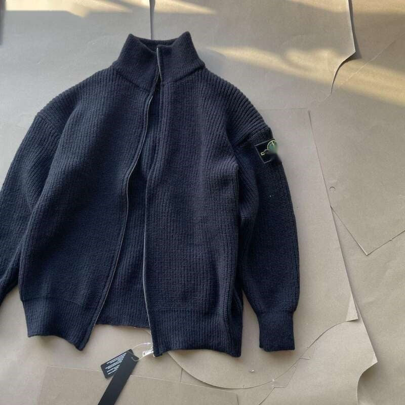 A dark navy blue ribbed knit zip-up jacket with a mock neck collar, laid flat on a beige cardboard background. A small green and black Stone Island compass patch is visible on the upper left sleeve.