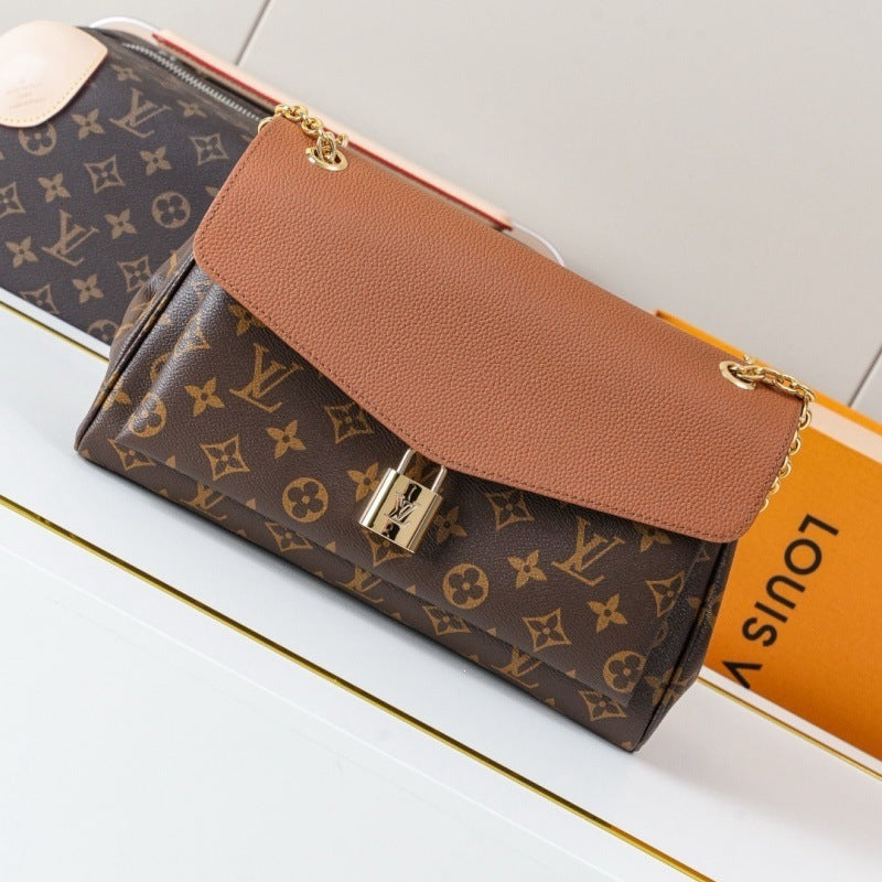 Louis Vuitton monogram canvas shoulder bag with a tan leather flap and gold-tone hardware, shown on a white surface with part of an orange Louis Vuitton box visible.