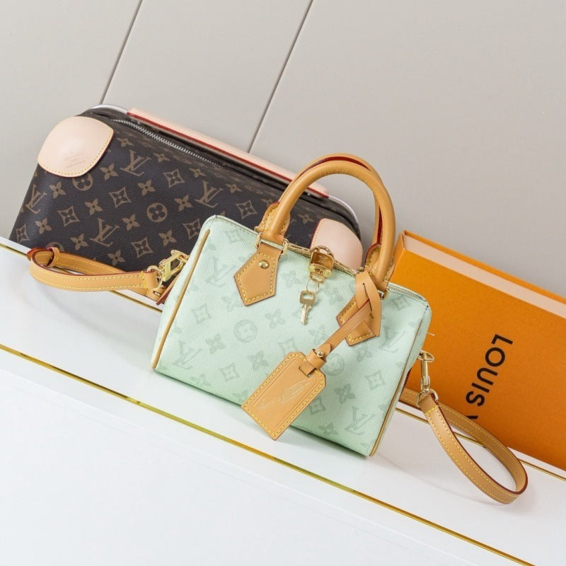 A Louis Vuitton handbag arranged on a white surface with a monogram pouch behind it and an orange Louis Vuitton box to the right. The main product is a small light mint green monogram handbag with tan leather handles, trim, and strap, plus gold-tone hardware.