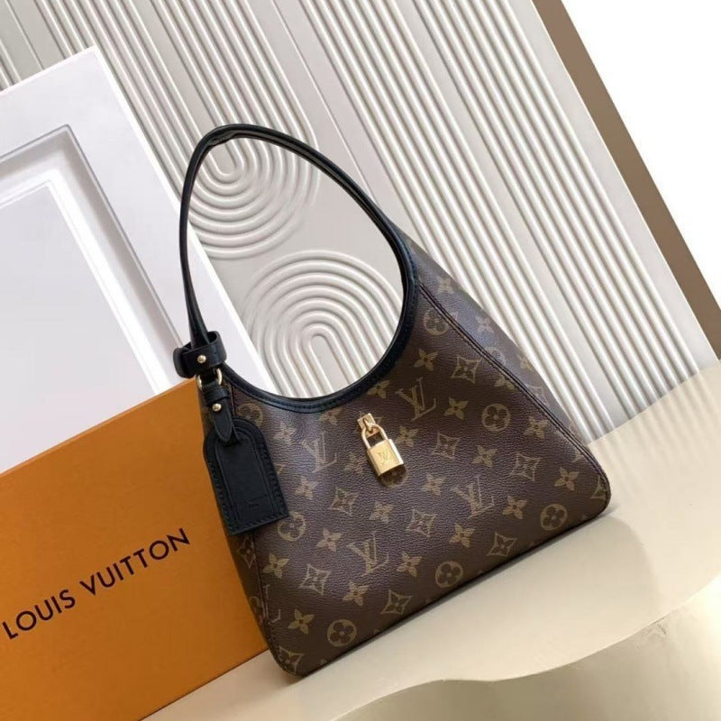 Louis Vuitton monogram shoulder bag in brown coated canvas with black leather trim and handle, shown beside an orange Louis Vuitton box on a light beige surface.