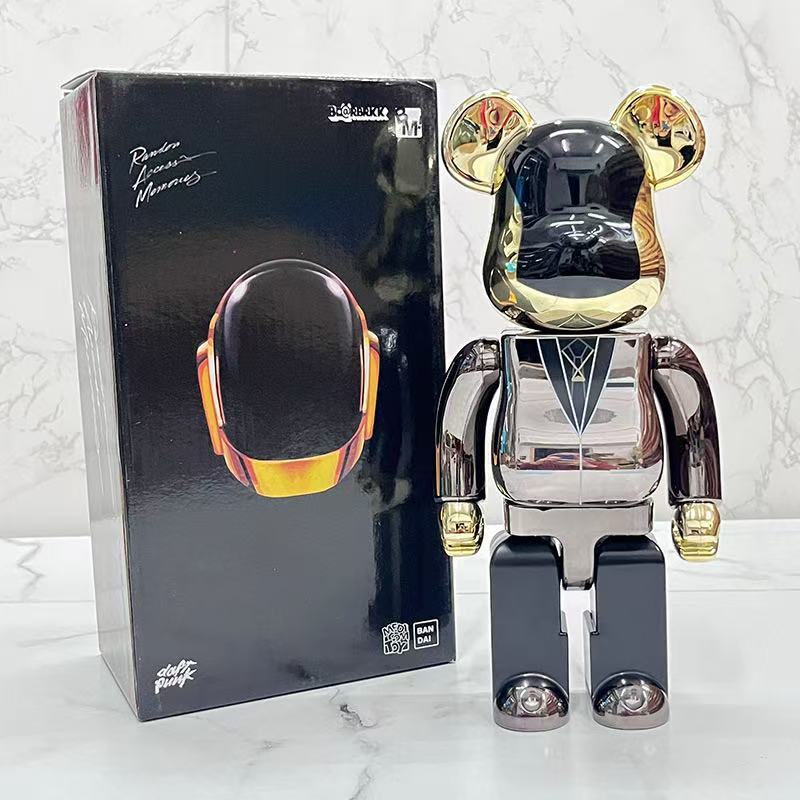A metallic bear-shaped collectible figure with a glossy black and chrome silver body and gold accents stands next to its black retail box on a light marble surface.