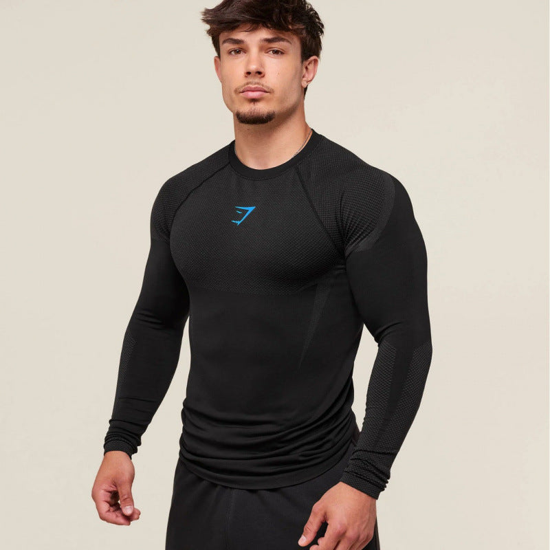 Man wearing a black long-sleeve athletic shirt with a blue logo on a beige background