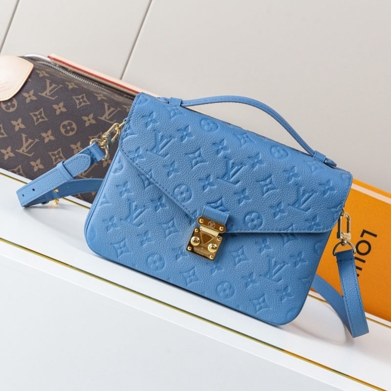 A light blue Louis Vuitton monogram embossed leather shoulder bag with a gold-tone lock, displayed on a white surface next to a Louis Vuitton monogram pouch and an orange box.
