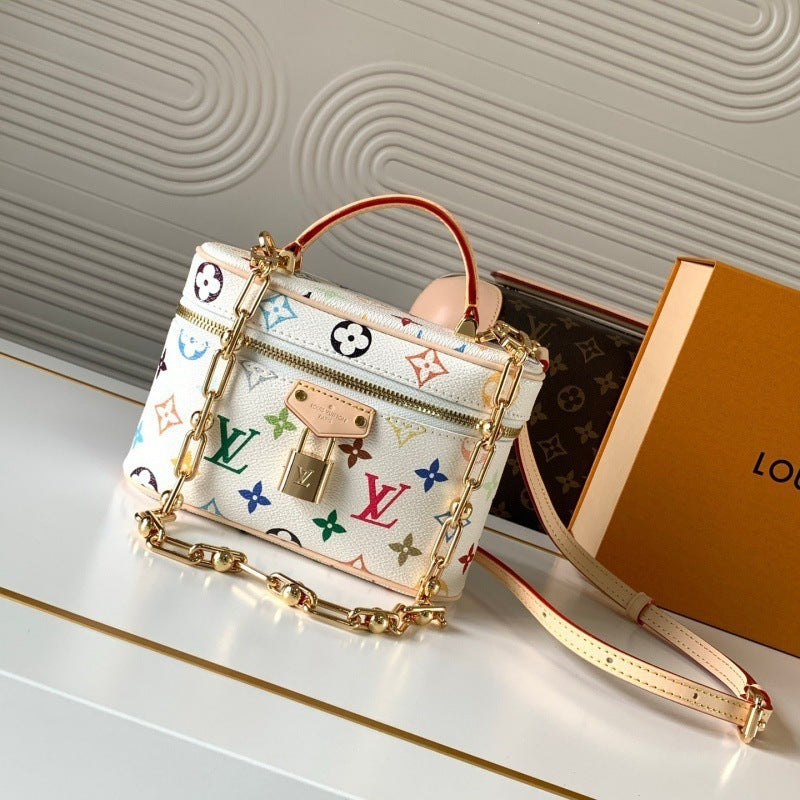 A Louis Vuitton mini top-handle bag in white coated canvas with a colorful monogram print, gold-tone chain strap, and lock closure, displayed next to its orange and brown monogram box on a light surface.