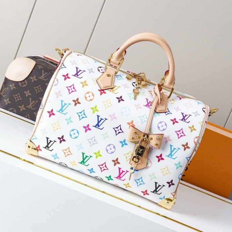 A Louis Vuitton Speedy bag in multicolor pastel monogram canvas with tan leather handles and a bow charm, displayed on a white shelf next to another bag.