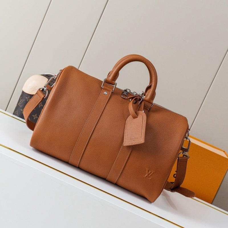 A Louis Vuitton tan leather Speedy bag with a top handle, leather tag, and side strap, displayed on a white shelf next to an orange box.