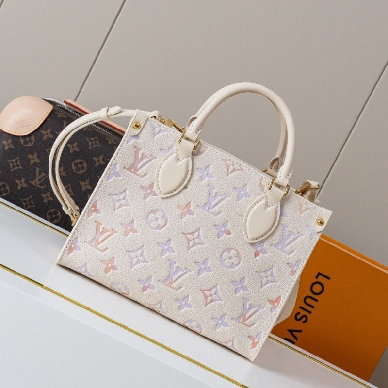 A Louis Vuitton handbag in off-white monogram canvas with pastel pink, blue, and purple monogram motifs, displayed on a white surface next to a Louis Vuitton box.