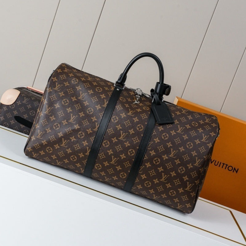 Louis Vuitton monogram canvas duffel bag with black leather handles and trim, displayed on a white surface next to an orange Louis Vuitton box.